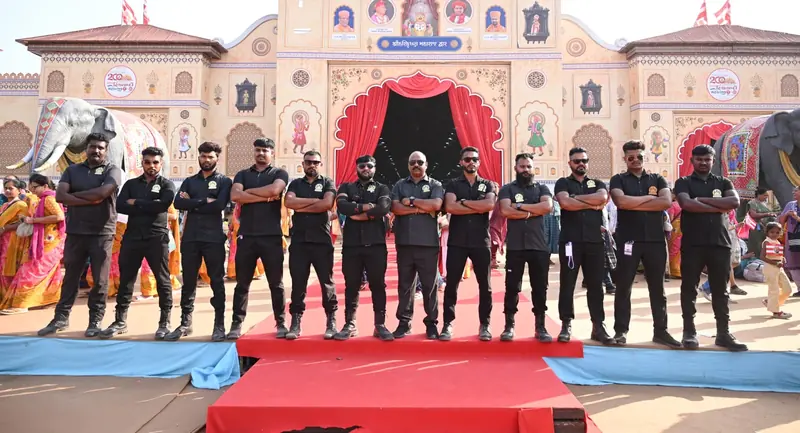Twelve Golden Hawk Security guards in black uniforms standing in a line on a red carpet in front of a decorated festival gate